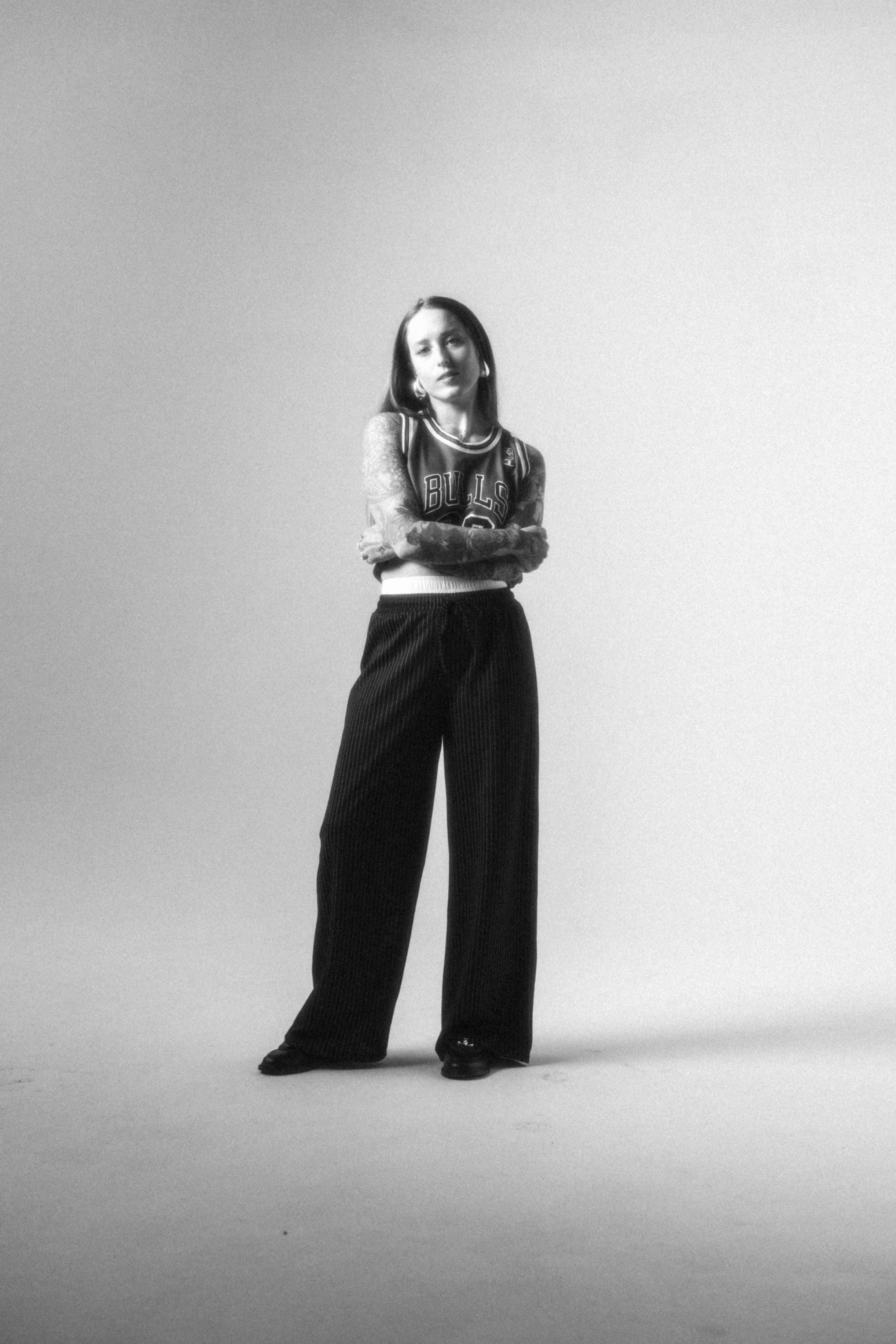 Full body professional photo of Libby Reese, in black-and-white. She’s wearing a fashionable outfit and has her arms crossed.